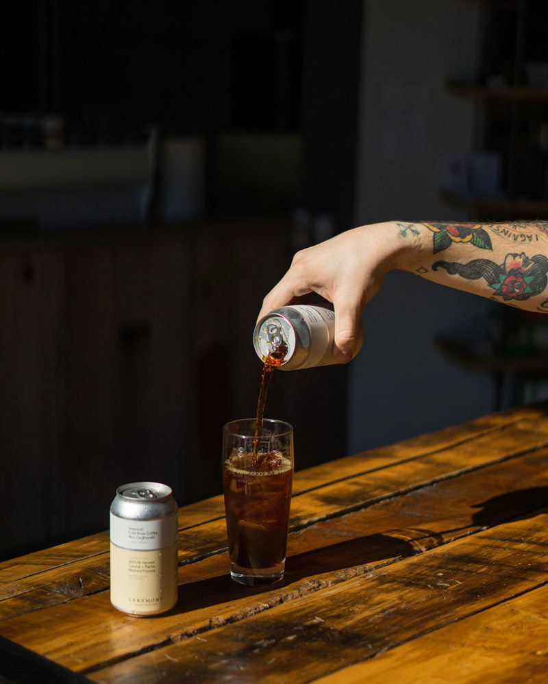 A tattooed arm pouring a cold brew can at the Roastery cafe location.