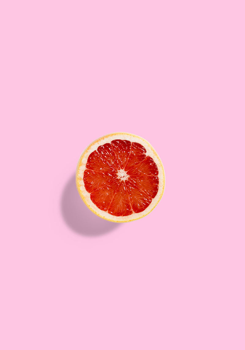 A top-down view of a sliced red grapefruit centered on a solid pink background with a soft shadow.