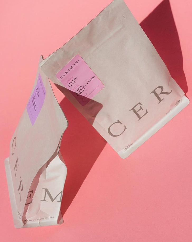 Two beige coffee bags with purple labels, reading  CEREMONY  on a pink background with shadows cast to the right.